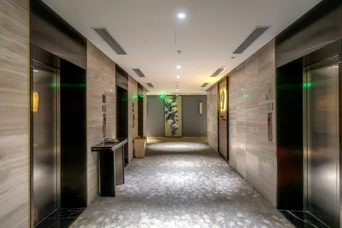 A hotel elevator lobby with stone-look wall panels, steel elevator doors and patterned carpet